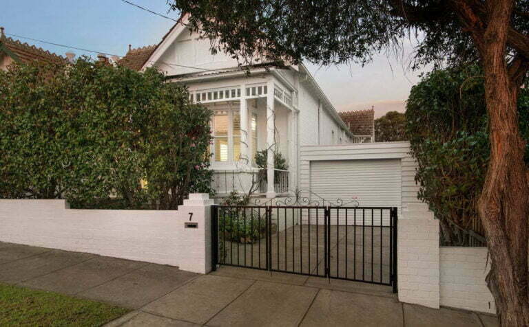 A white weatherboard house with white brickwork and a black wireframe gate.