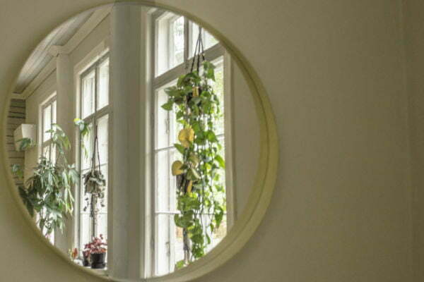 An indoor photo taken of a round miror reflecting windows with plants sitting on the windows sill.