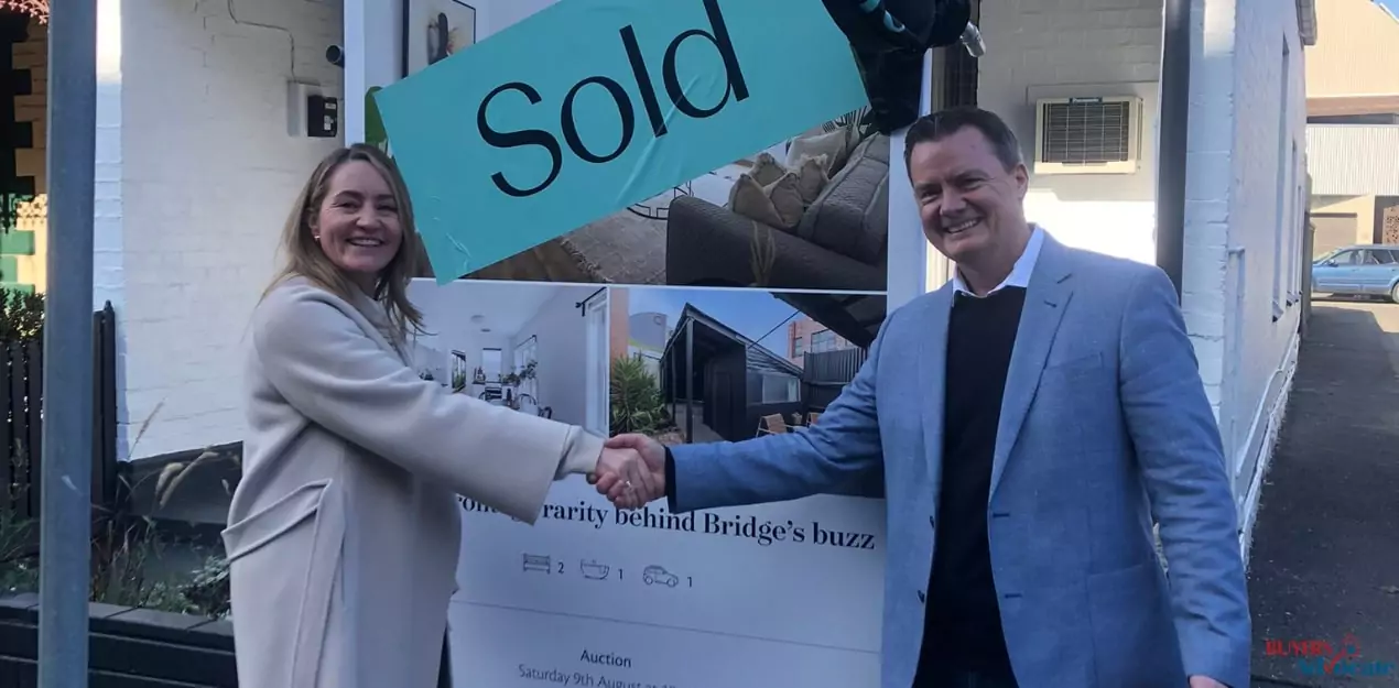 A smiling property manager shaking hands with client in front of a sold sign in Melbourne.