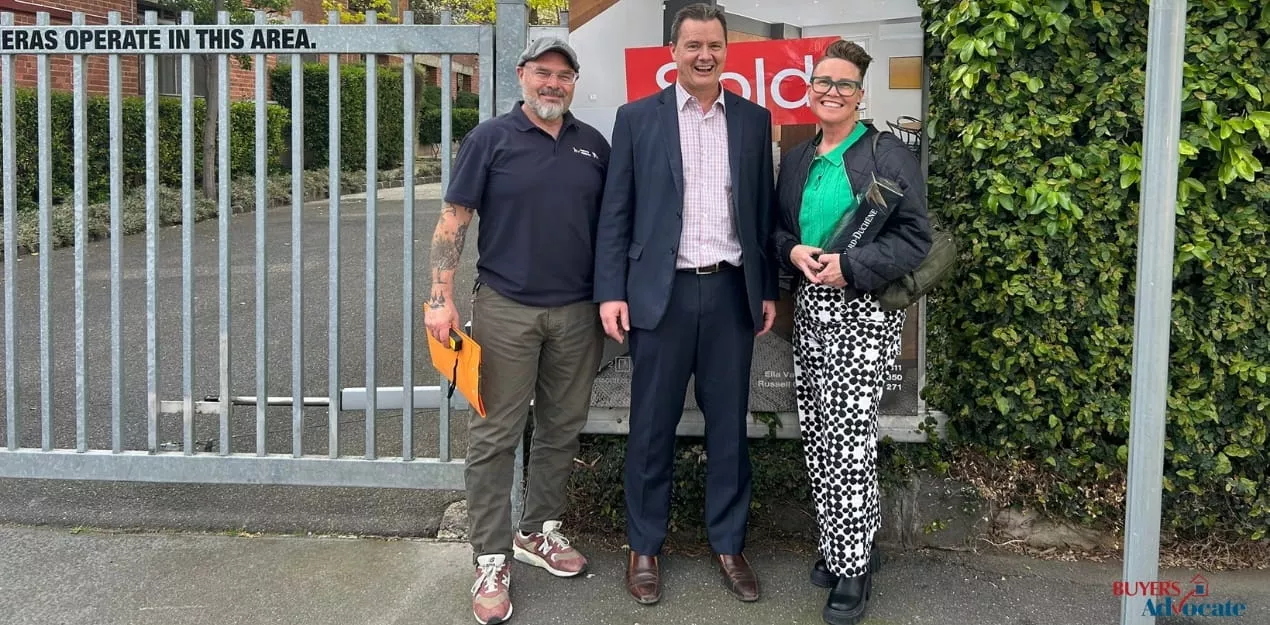 Three people standing beside a sold sign following a Melbourne property sale.